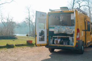 Yellow van with rear doors open revealing a campervan interior. Green grass and Autumn trees in the background