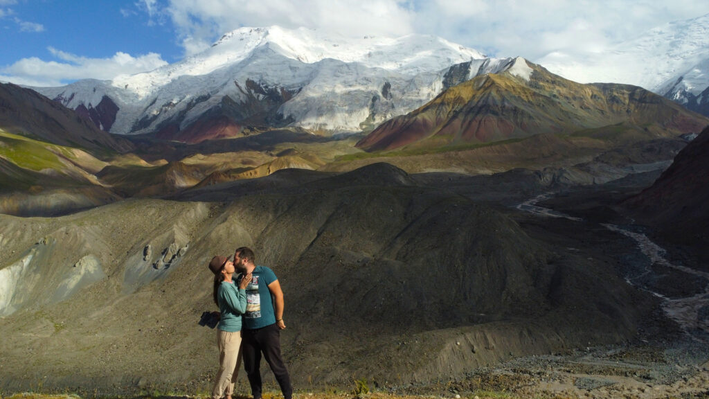 A couple sharing a kiss with a stunning mountain range in the background, capturing a romantic moment in nature.