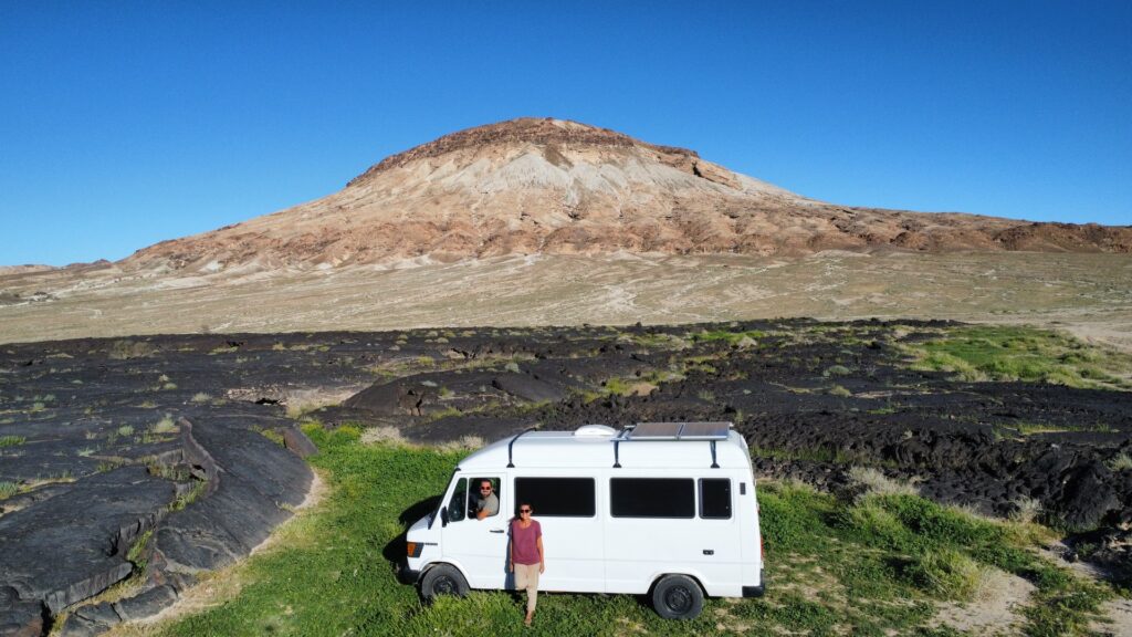 A person stands beside a white van, with a majestic mountain backdrop in clear view.